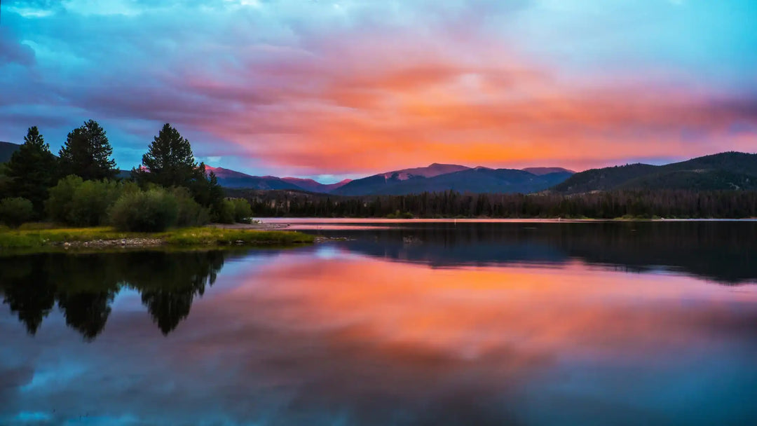 Tranquil lake reflecting a vibrant sunset sky and silhouetted mountains.