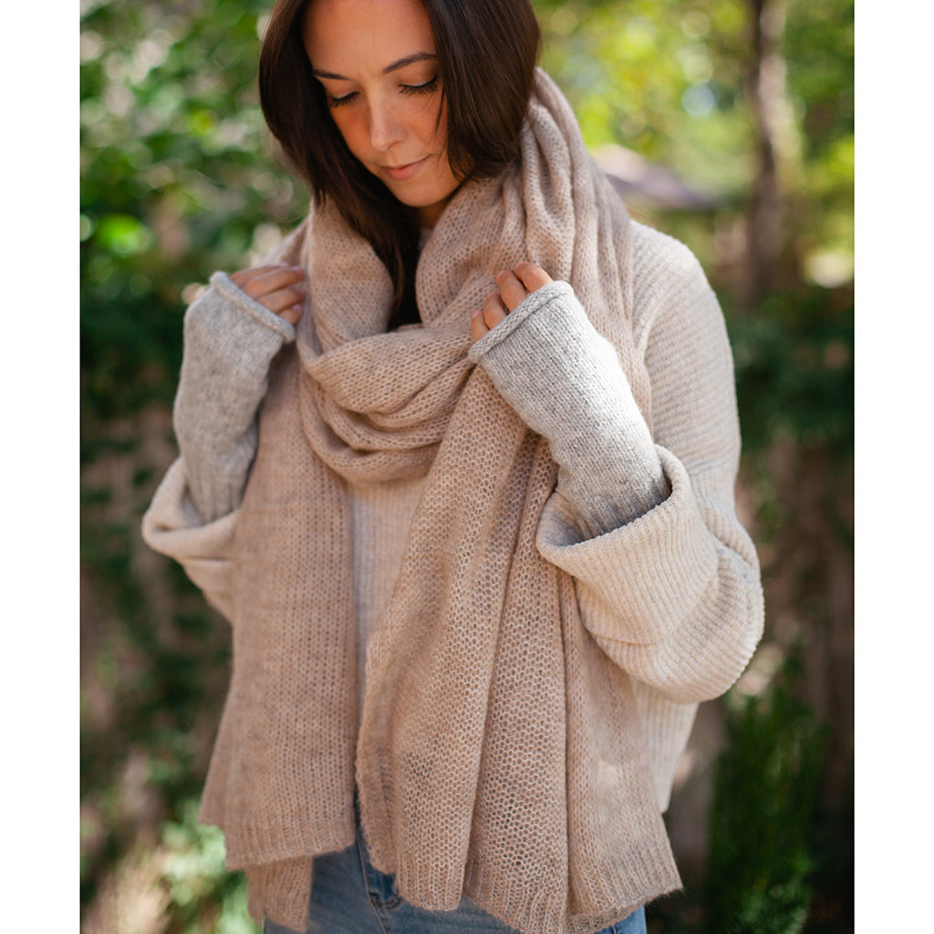 Model wearing soft beige alpaca and merino blend knit scarf displayed with gloves and a hat