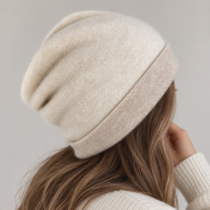 A person shown from the back wearing a soft slouchy knit cashmere beanie in a warm off-white/cream tone, with long light brown hair and a matching cream ribbed sweater against a plain light gray background.