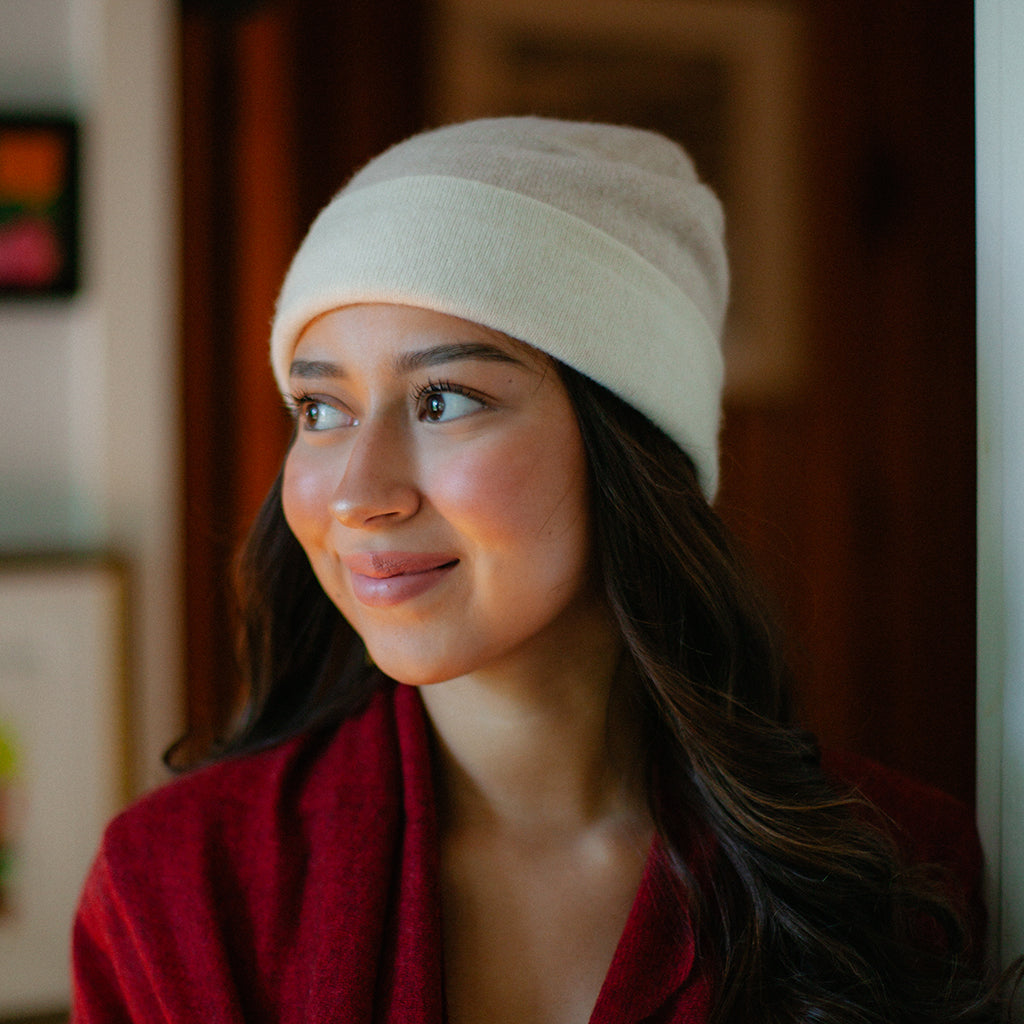 A woman wearing a cream-colored knit beanie and a red top, looking to the side in an indoor setting.
