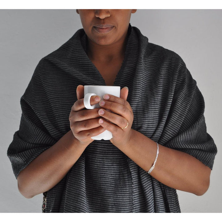 Male model with dark French gray striped cotton scarf/wrap wrapped around his shoulders,  holding a mug